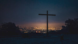 A silhouette of a cross at sunset with the lights of a city in a valley beyond